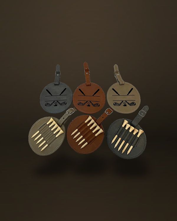 Six round faux-leather golf bag tags with buckle straps, three engraved with crossed golf clubs above a blank name panel and three turned over to show wooden tees held in a strap.