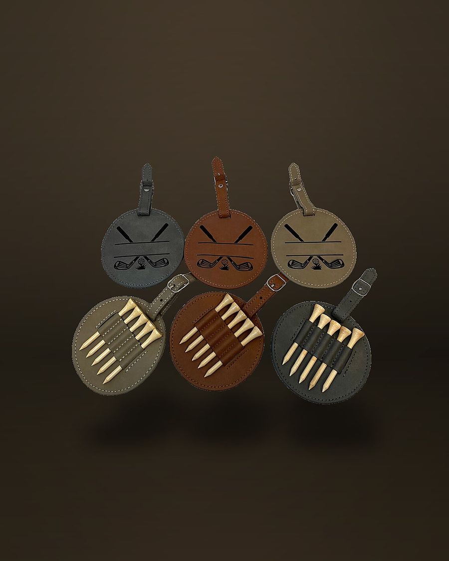 Six round faux-leather golf bag tags with buckle straps, three engraved with crossed golf clubs above a blank name panel.
