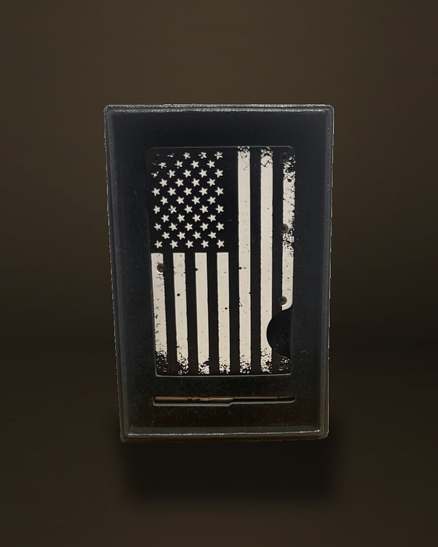 A black metal RFID card-holder wallet engraved with a distressed American flag, standing upright in its open gift box.
